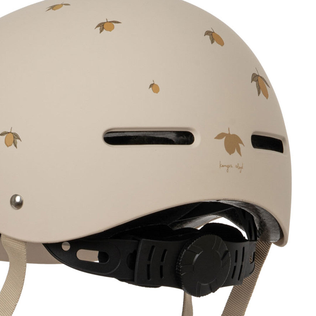 Detail van de Konges Sløjd kinderhelm in beige met citroenpatroon en het merklogo.