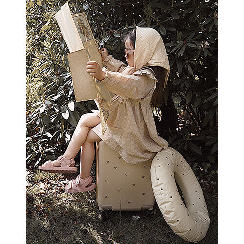 Een kind zit buiten op de beige kinderkoffer met kersenpatroon en leest een boek.