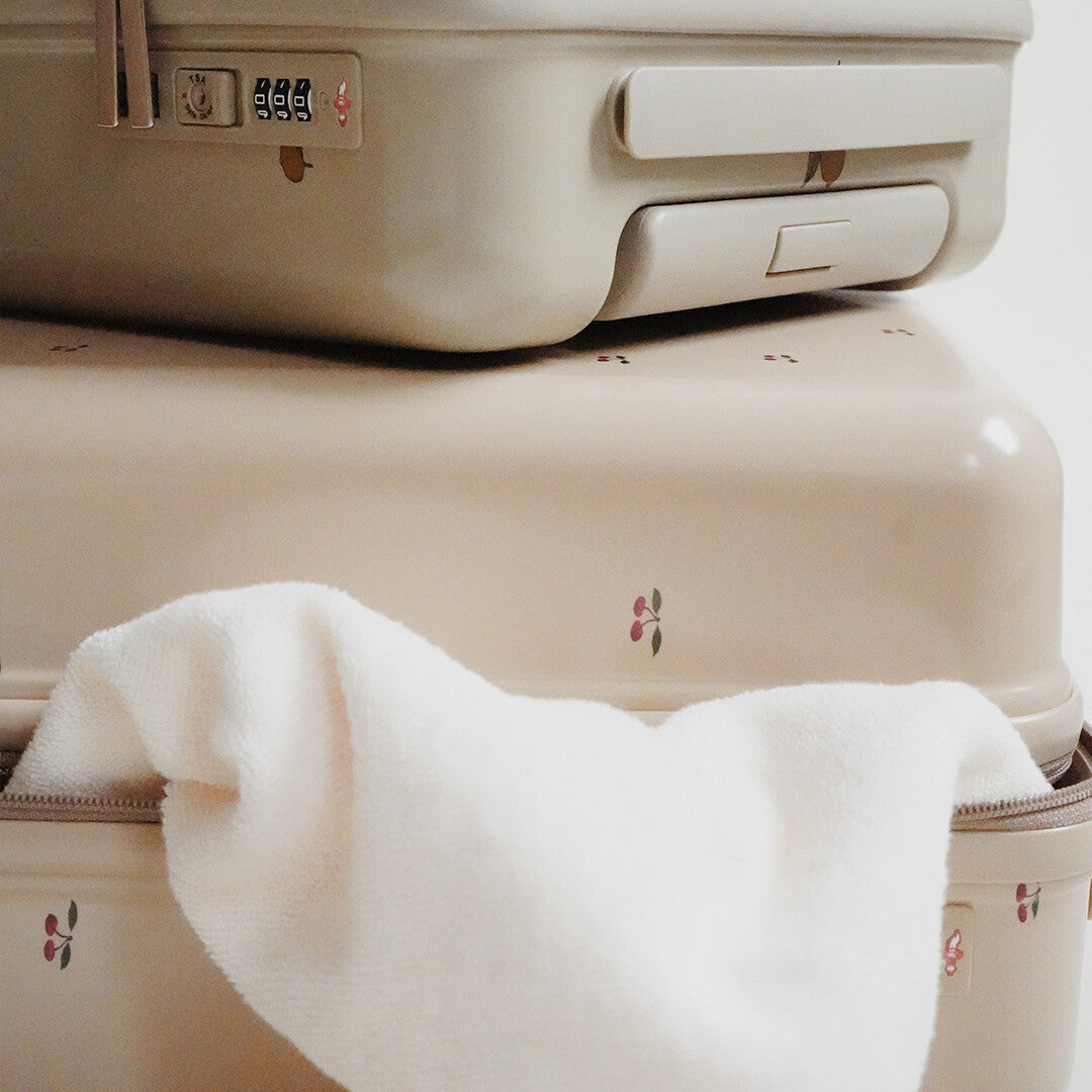 Detail van twee gestapelde beige kinderkoffers met kersenpatroon, met een witte handdoek die uit de onderste steekt.