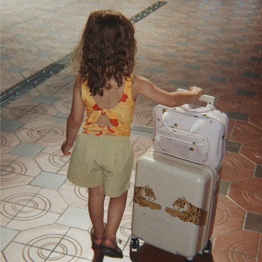 Een kind trekt de beige kinderkoffer met tijgerprint en een roze tasje over een tegelvloer.