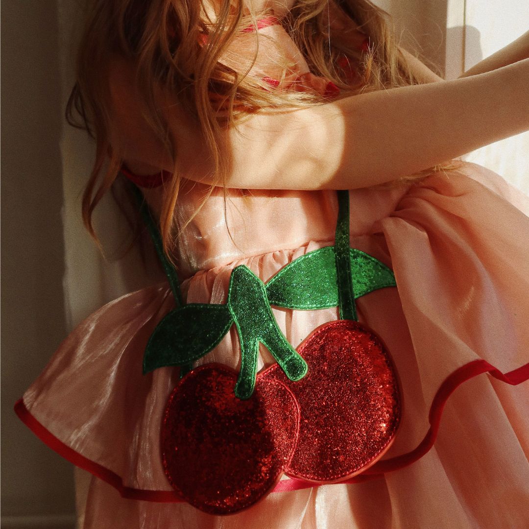 Een kind draagt de glitter kersentas over een roze jurk.