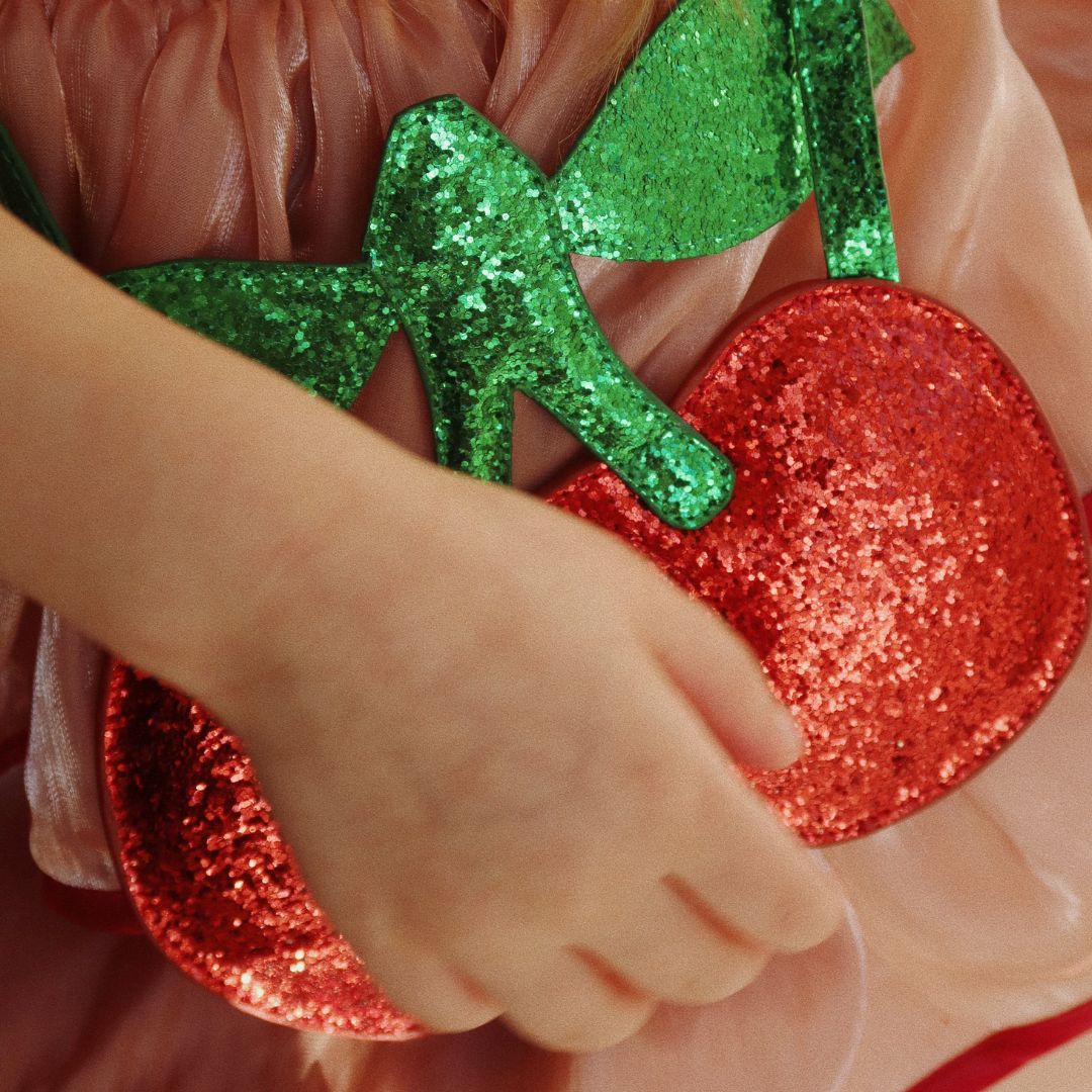 Een kinderhand houdt de rode glitter kersentas vast.