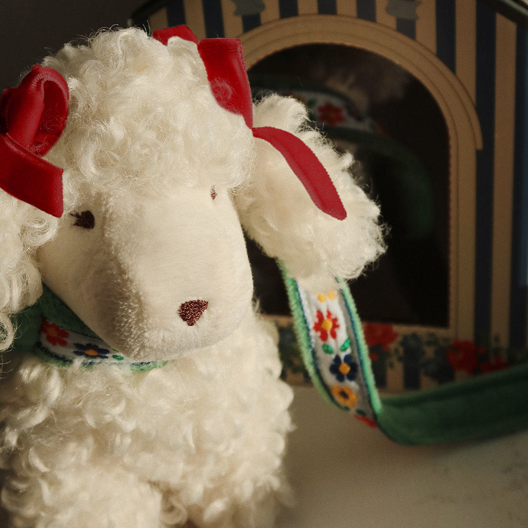 Detailopname van de Konges Sløjd witte pluchen poedel knuffelpuppy met rode strikjes en bloemenhalsband.