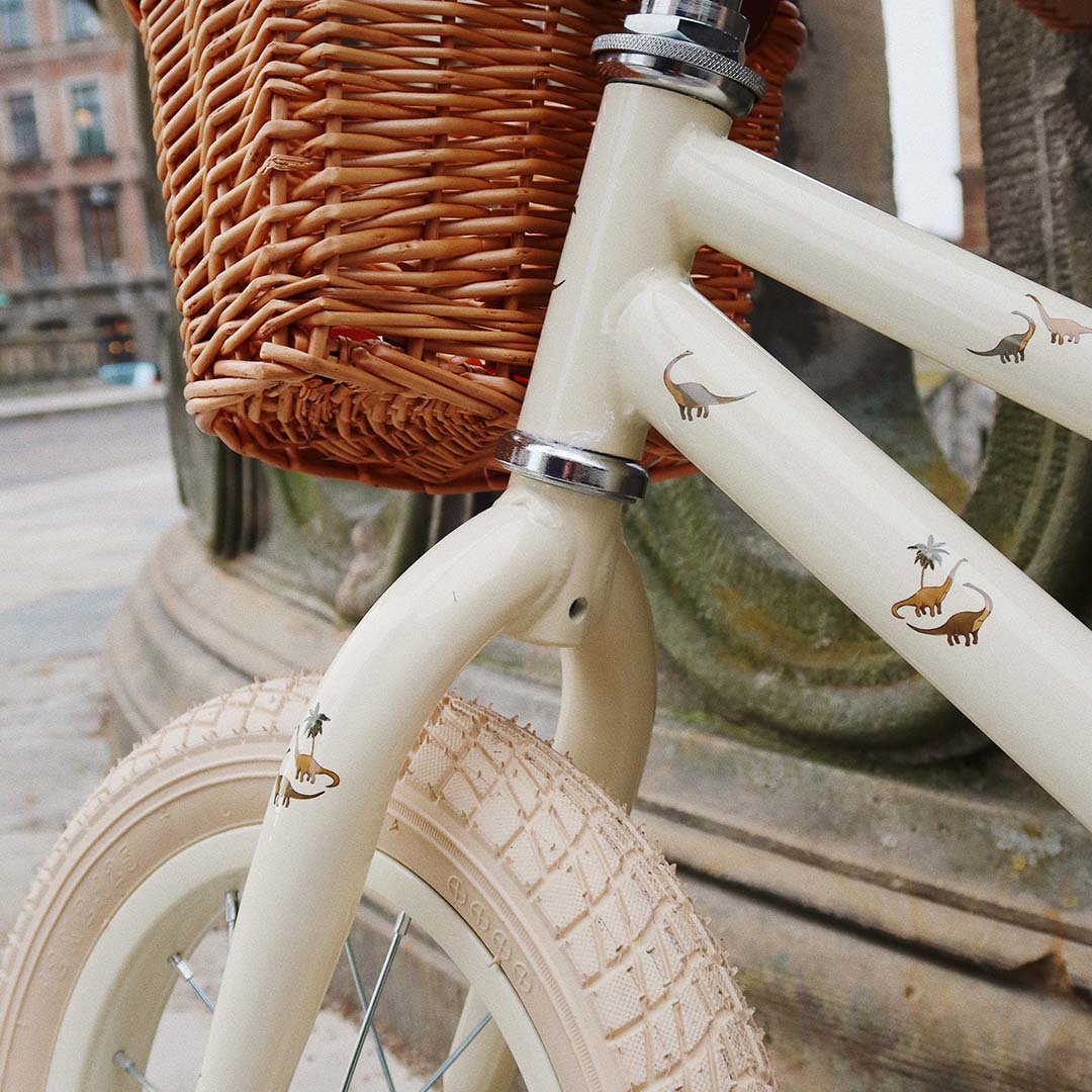 Detail van de Konges Sløjd loopfiets met dinosaurusfiguren op het beige frame en een rotan mandje.