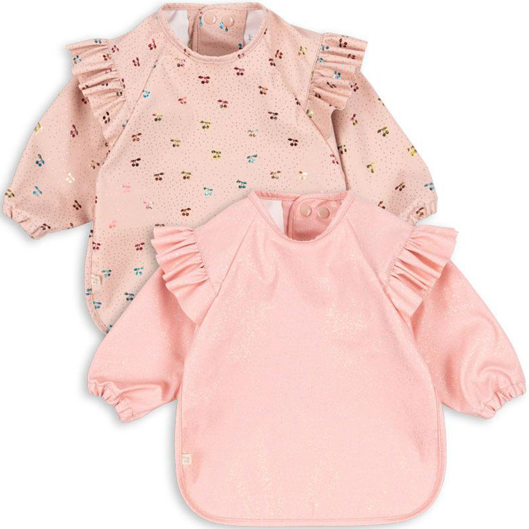 Twee roze Konges Sløjd mouwslabben voor baby's, één met kersenprint en één effen roze met glitters.