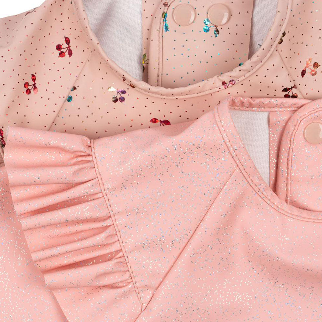Detailfoto van twee roze Konges Sløjd mouwslabben met ruches en glitters, één met kersenprint.
