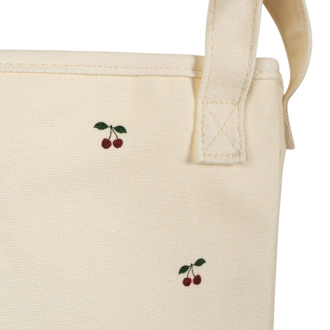 Detail van een beige katoenen opbergmand met kersenpatroon en handvat.