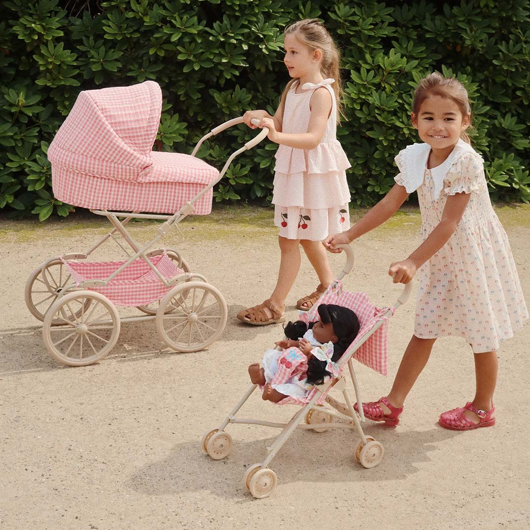 Twee kinderen lopen met een Konges Sløjd poppenbuggy en een bijpassende poppenwagen over een grindpad.