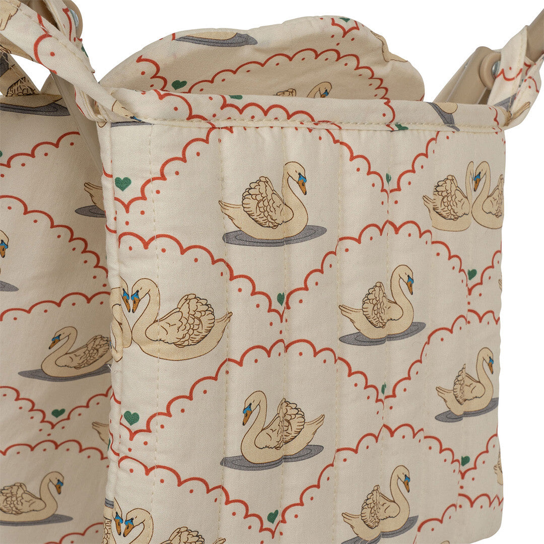 Close-up van de beige stof van de poppenbuggy met een gedetailleerd zwanenpatroon.