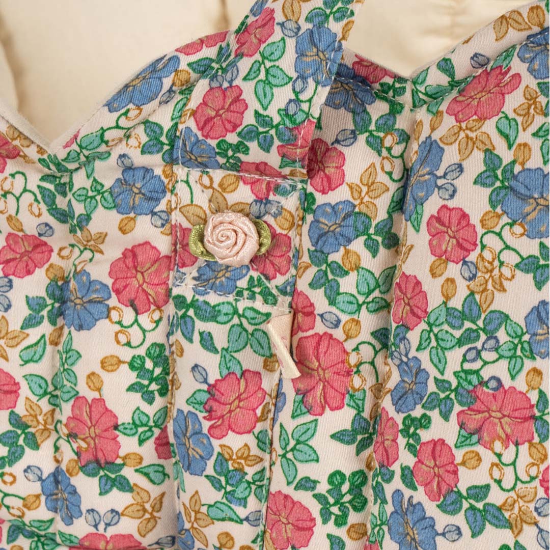 Detail van de gebloemde stof van de poppenreiswieg met een roze roosje als knoop.