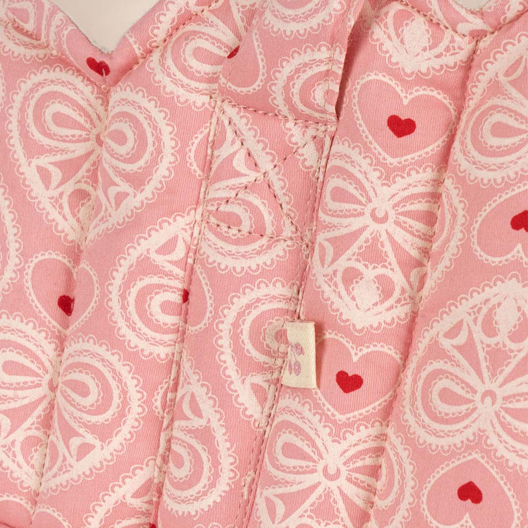 Detail van de roze stof van de poppenreiswieg met wit kant en rode harten.