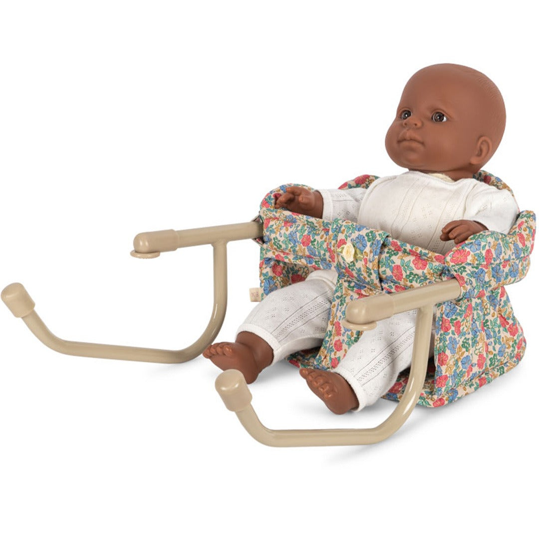 Konges Sløjd poppentafelstoel met gebloemd patroon, waarin een pop met donkere huidskleur zit.