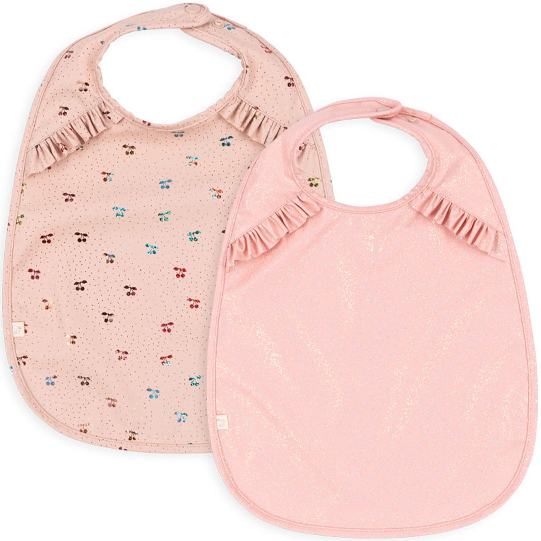 Konges Sløjd set van twee roze babyslabbetjes, één met kersenpatroon en één met glitters.