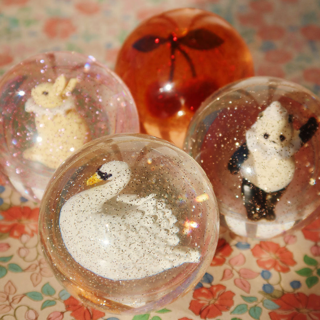 Vier stuiterballen met glitters en figuren van een konijn, panda, zwaan en kers op een bloemige ondergrond.