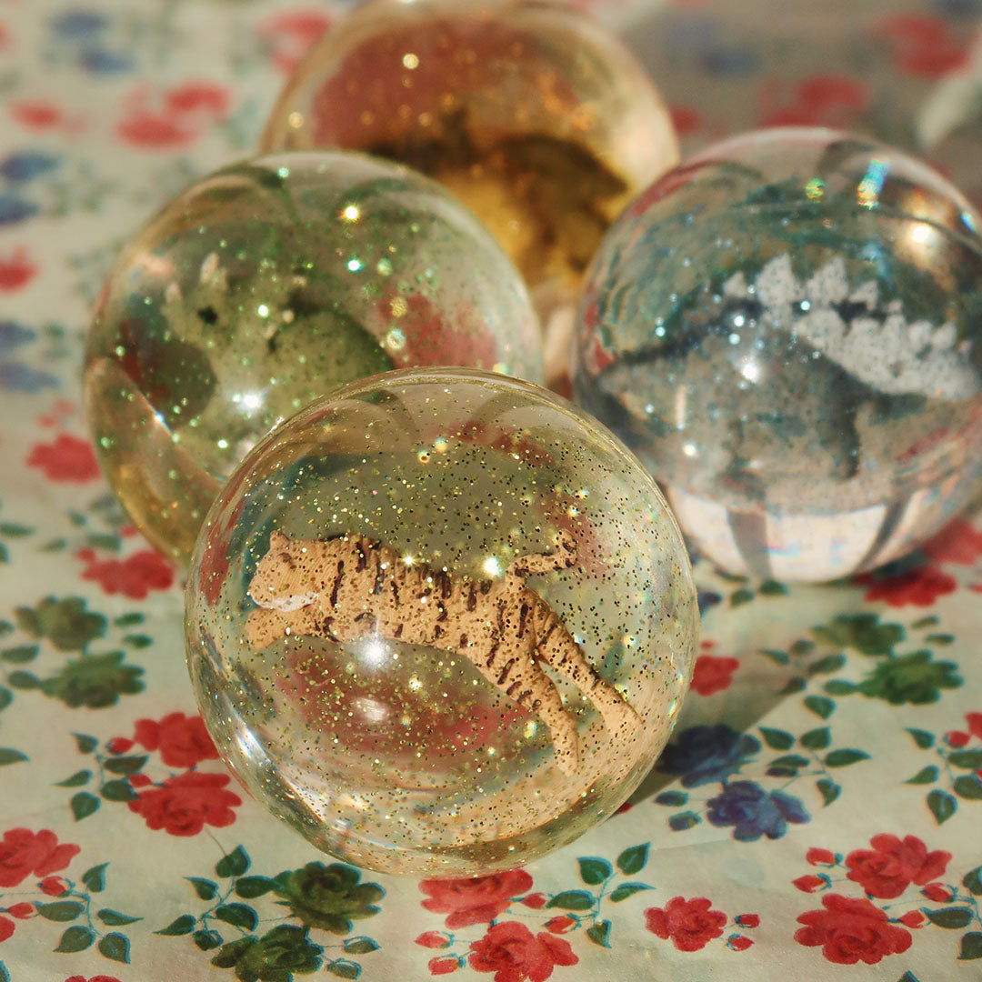 Vier stuiterballen met glitter en dierenfiguren, waaronder een tijger, op een bloemige ondergrond.