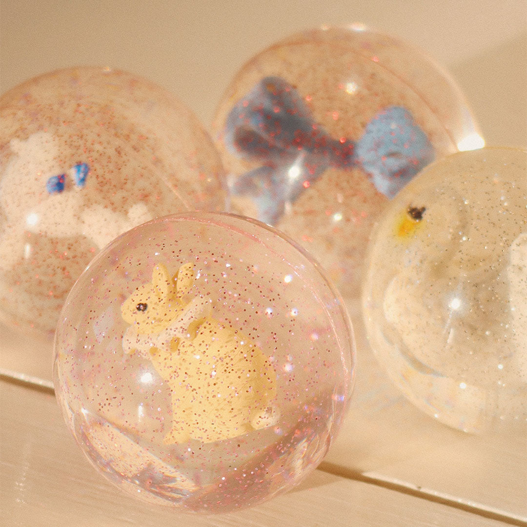 Een stuiterbal met glitters en een gele poedel erin, met andere stuiterballen op de achtergrond.