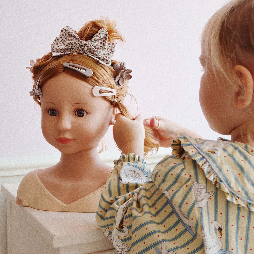 Een kind stylet het haar van de styling pop met bloemenstrik en haarclips.