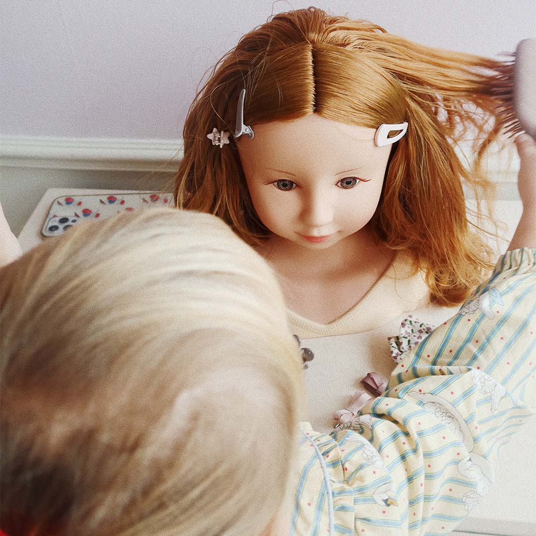 Een kind borstelt het lange bruine haar van de styling pop.