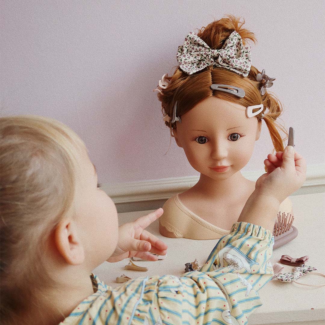 Een kind stylet het haar van de styling pop met een grote gebloemde strik en haarclips.