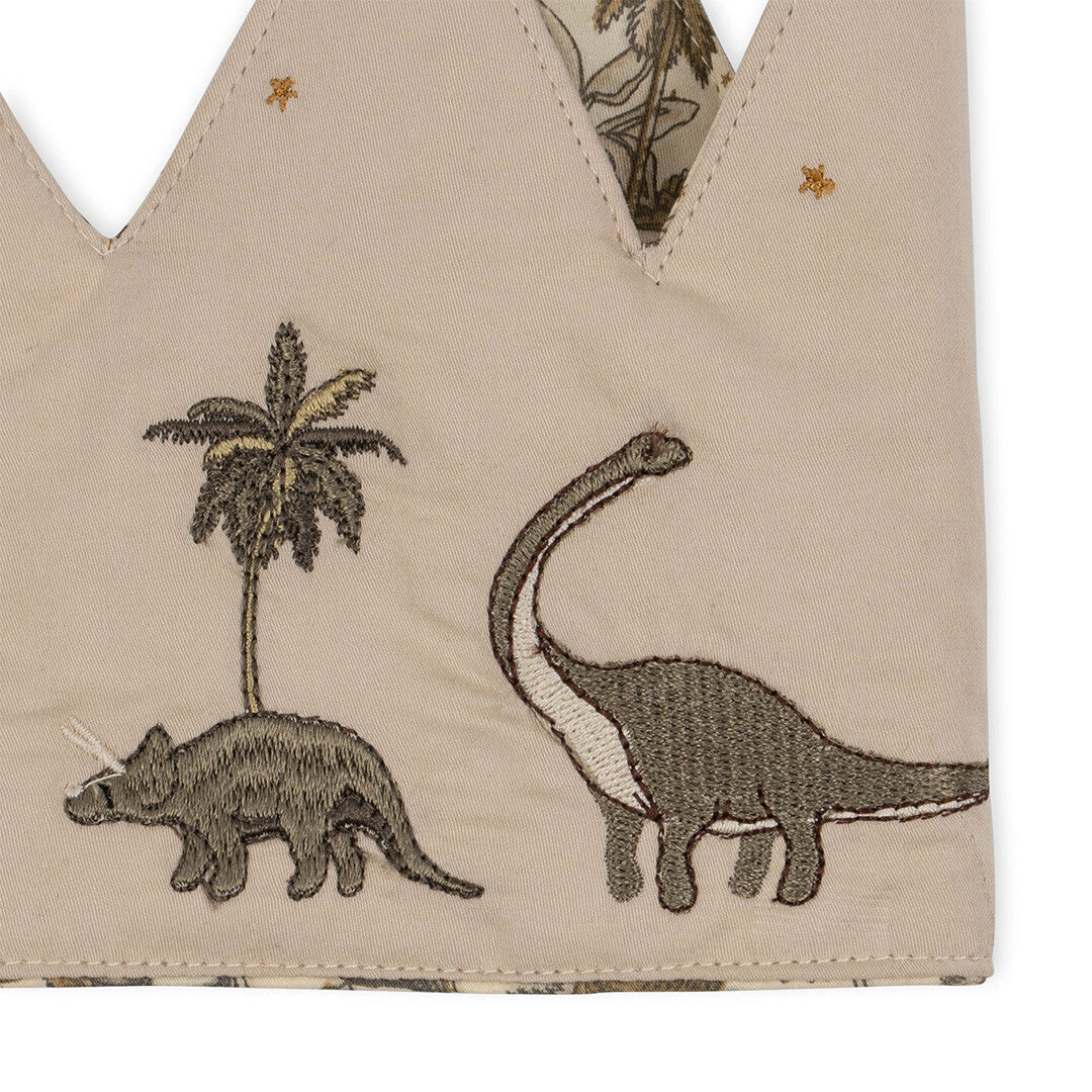 Detail van de Konges Sløjd verjaardagskroon met een geborduurde Triceratops en een langnekdinosaurus bij een palmboom.