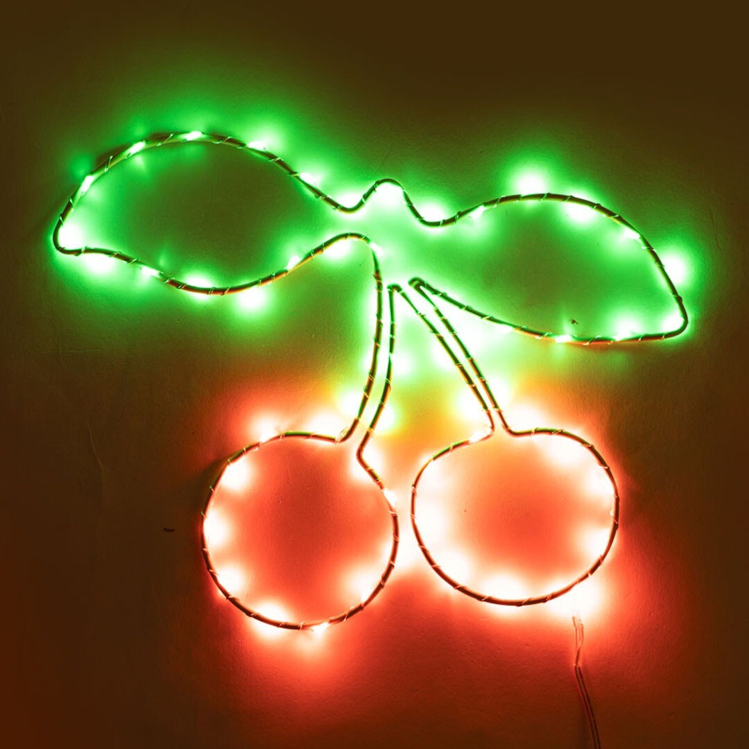 Konges Sløjd wandlamp in de vorm van kersen met groene bladeren, verlicht in rood en groen.