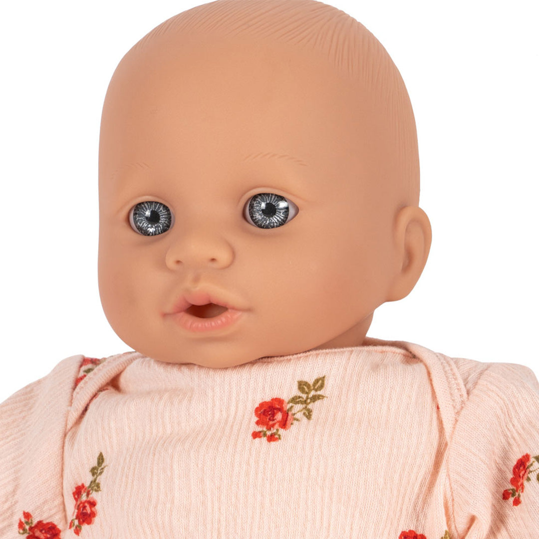 Close-up van het gezicht van de Konges Sløjd babypop Elisa met blauwe ogen en een roze gebloemd pakje.