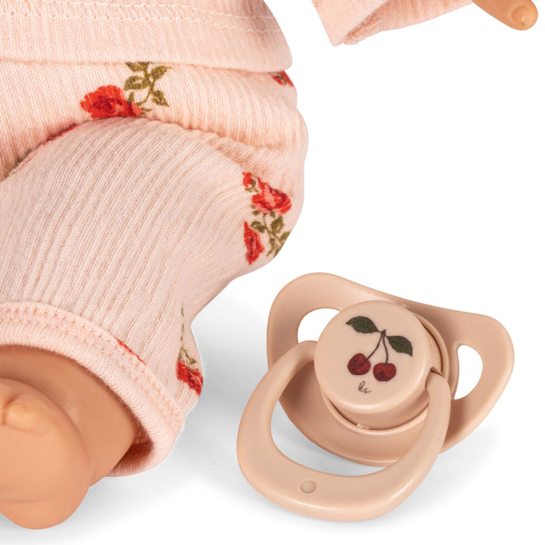 Detail van de Konges Sløjd babypop Elisa met roze gebloemd pakje en een losse speen met kersenmotief.