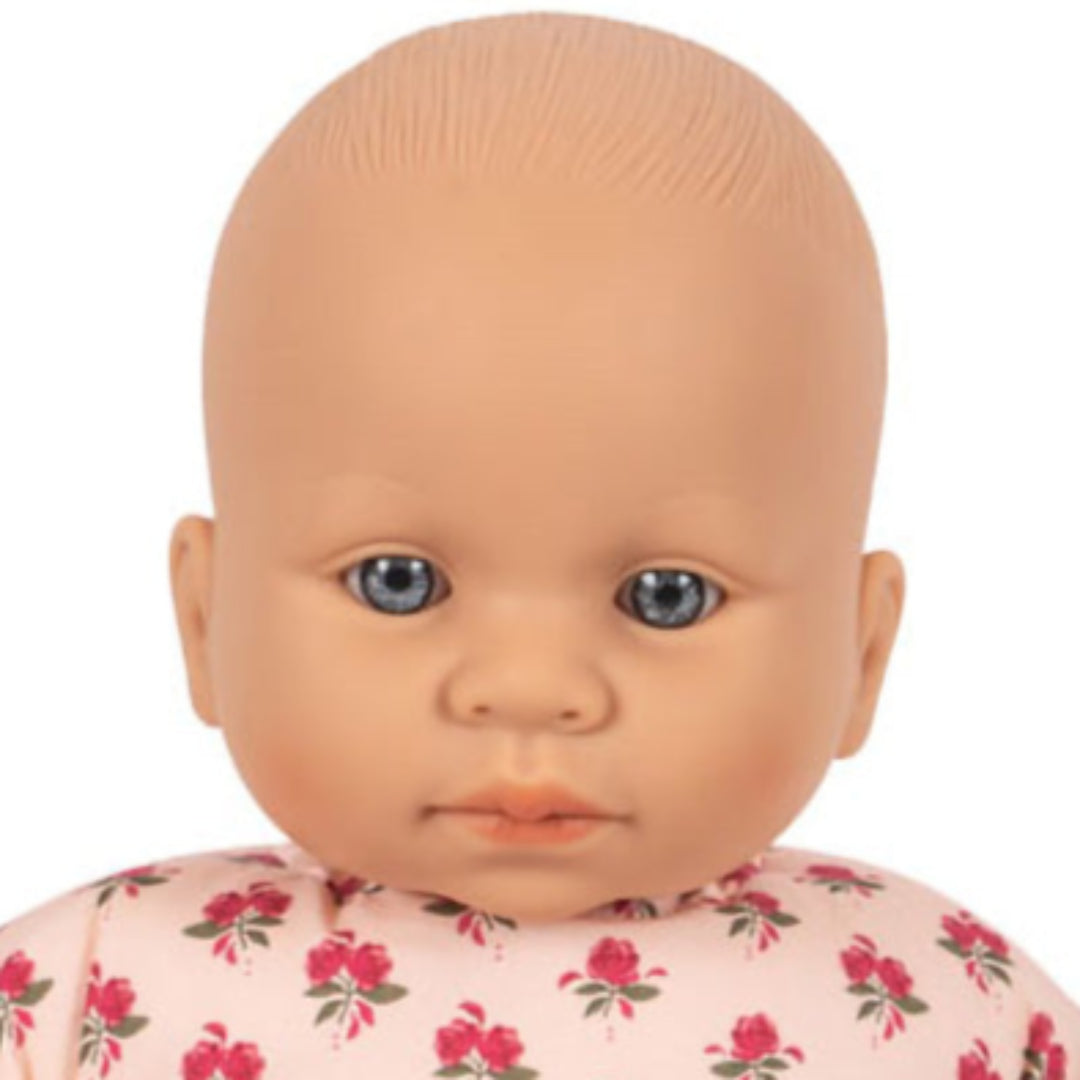 Detail van het gezicht van de Konges Sløjd babypop Kallis met blauwe ogen en roze gebloemde jurk.