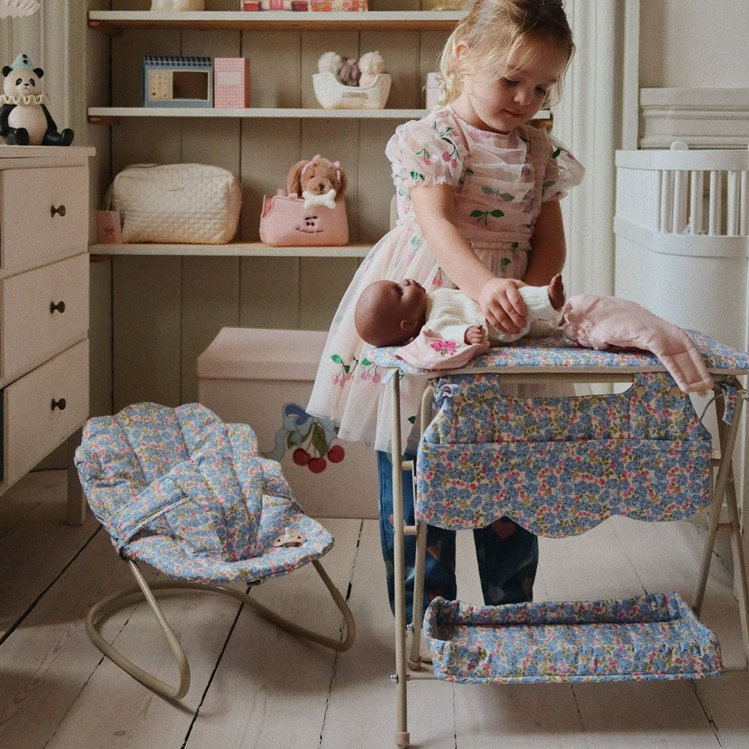 Een kind verschoont een pop op de Konges Sløjd poppenverschoontafel met gebloemd patroon in een kinderkamer.