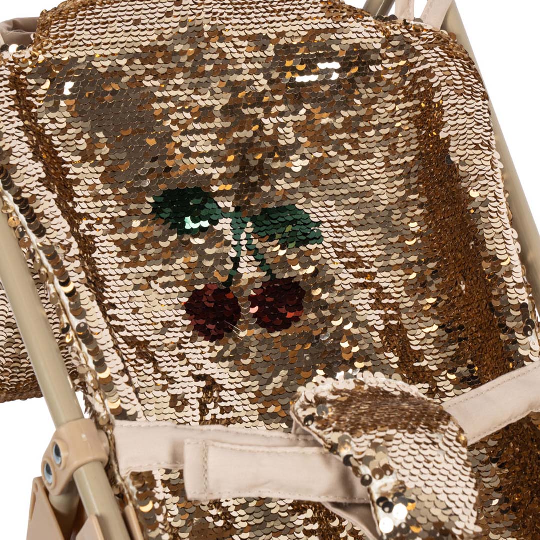 Detail van de gouden lovertjesstof van de poppenbuggy met een kersenpatroon.