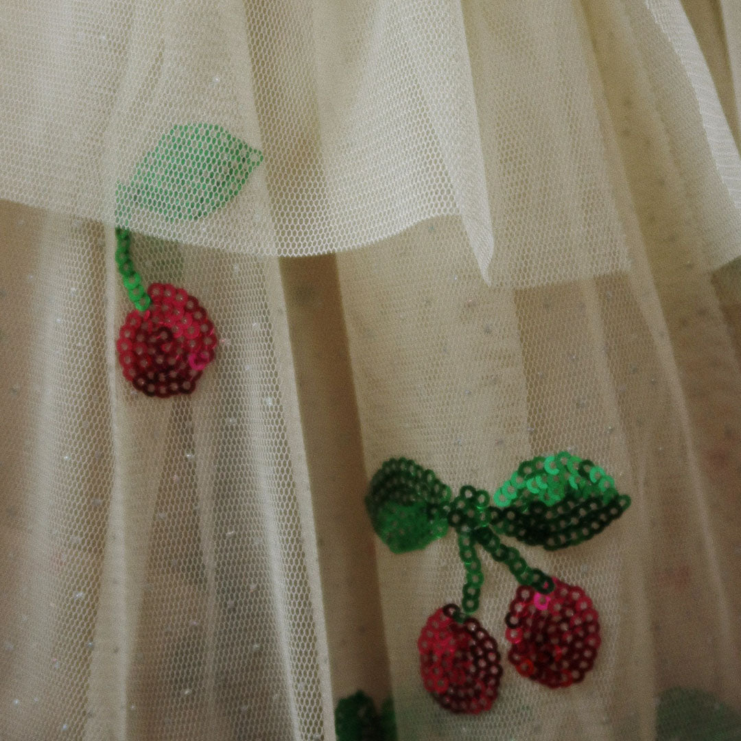 Detail van de beige stof van de verkleedcape met rode en groene kersenpailletten.