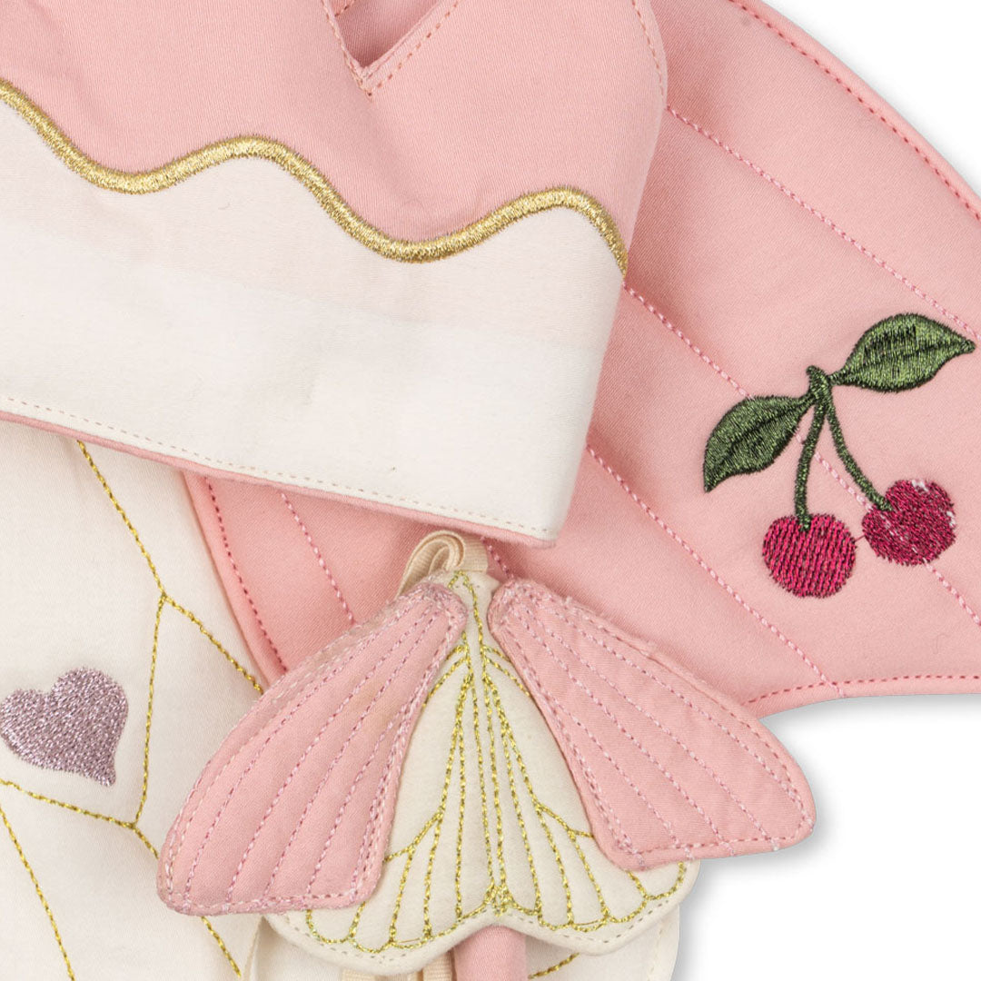 Detail van de roze en witte vlindervleugels met geborduurde kersen en harten, de kroon en de toverstaf.