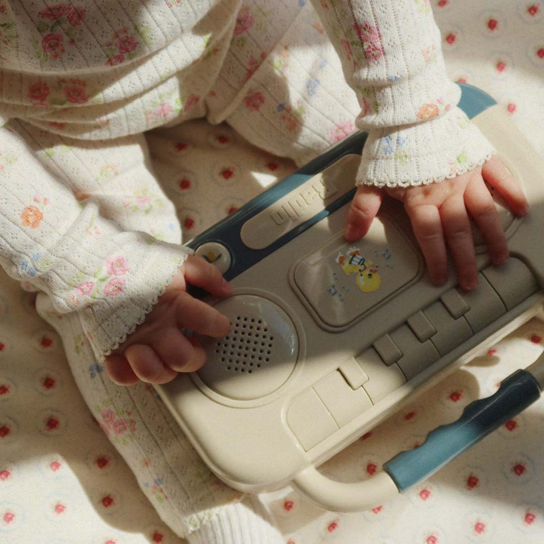 Babyhandjes in een bloemenpakje spelen met de voorkant van het Konges Sløjd muziekspeelgoed.