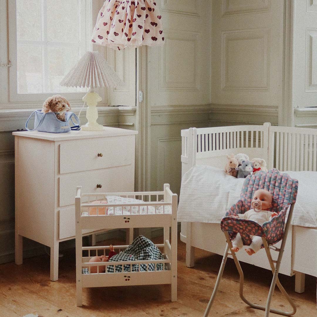 Een speelkamer met een Konges Sløjd babypop in een kinderstoel naast een poppenbedje en een commode.