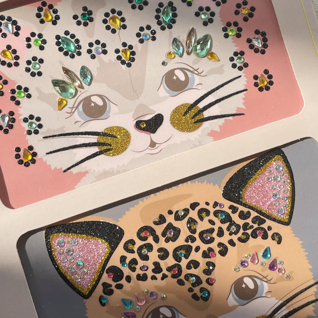 Detail van twee Konges Sløjd gezichtstickers met kattengezichten en glimmende juwelen.