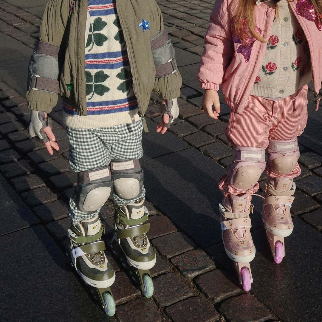 Twee kinderen met Konges Sløjd kinderskeelers en beschermers aan de benen, staand op kasseien.