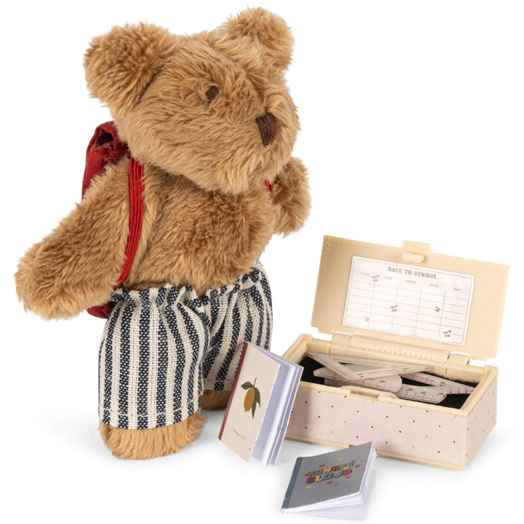 Konges Sløjd knuffelbeer Tiny Teddy met rode rugzak en gestreepte broek, naast een open doosje met miniatuur schoolspullen en notitieboekjes.