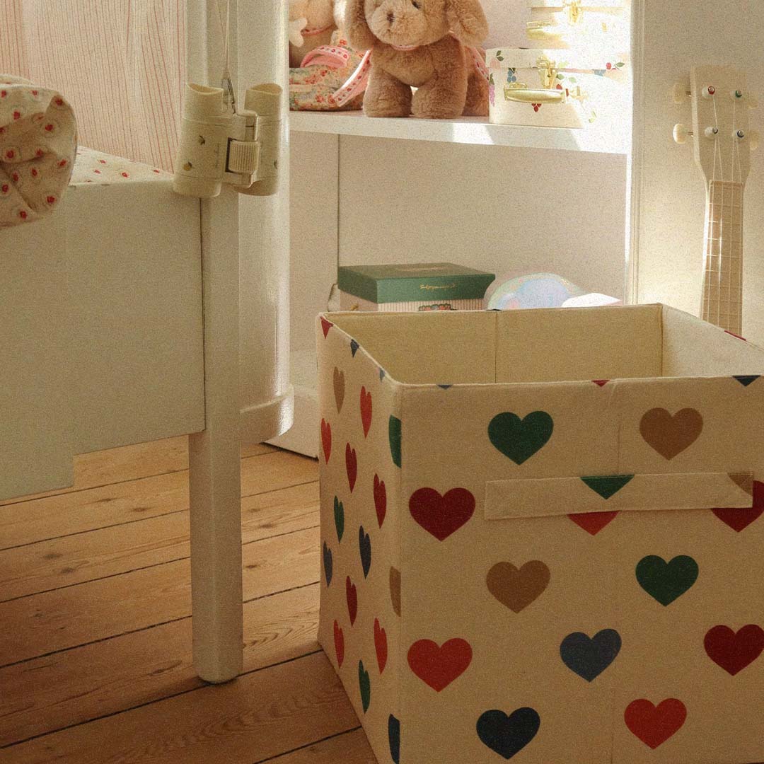 Een Konges Sløjd vierkante opbergmand met hartenpatroon staat op een houten vloer in een kinderkamer.