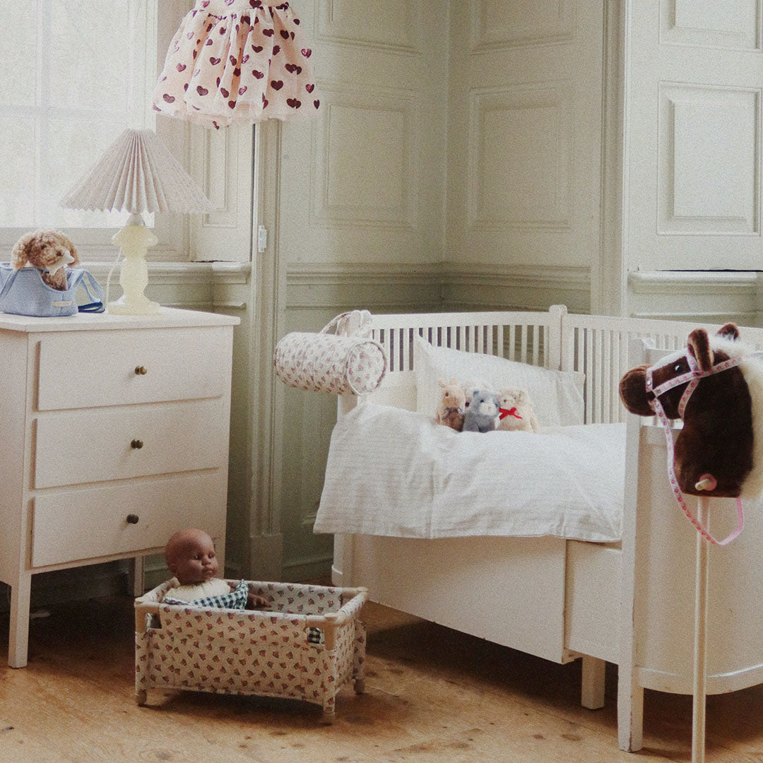 Een pop ligt in een poppenbed met gebloemd patroon in een kinderkamer.