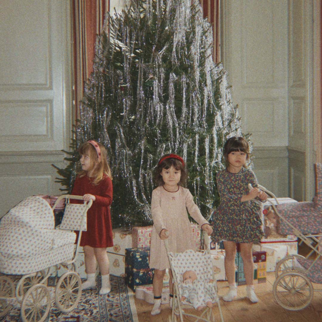 Drie meisjes spelen met poppenwagens voor een versierde kerstboom.