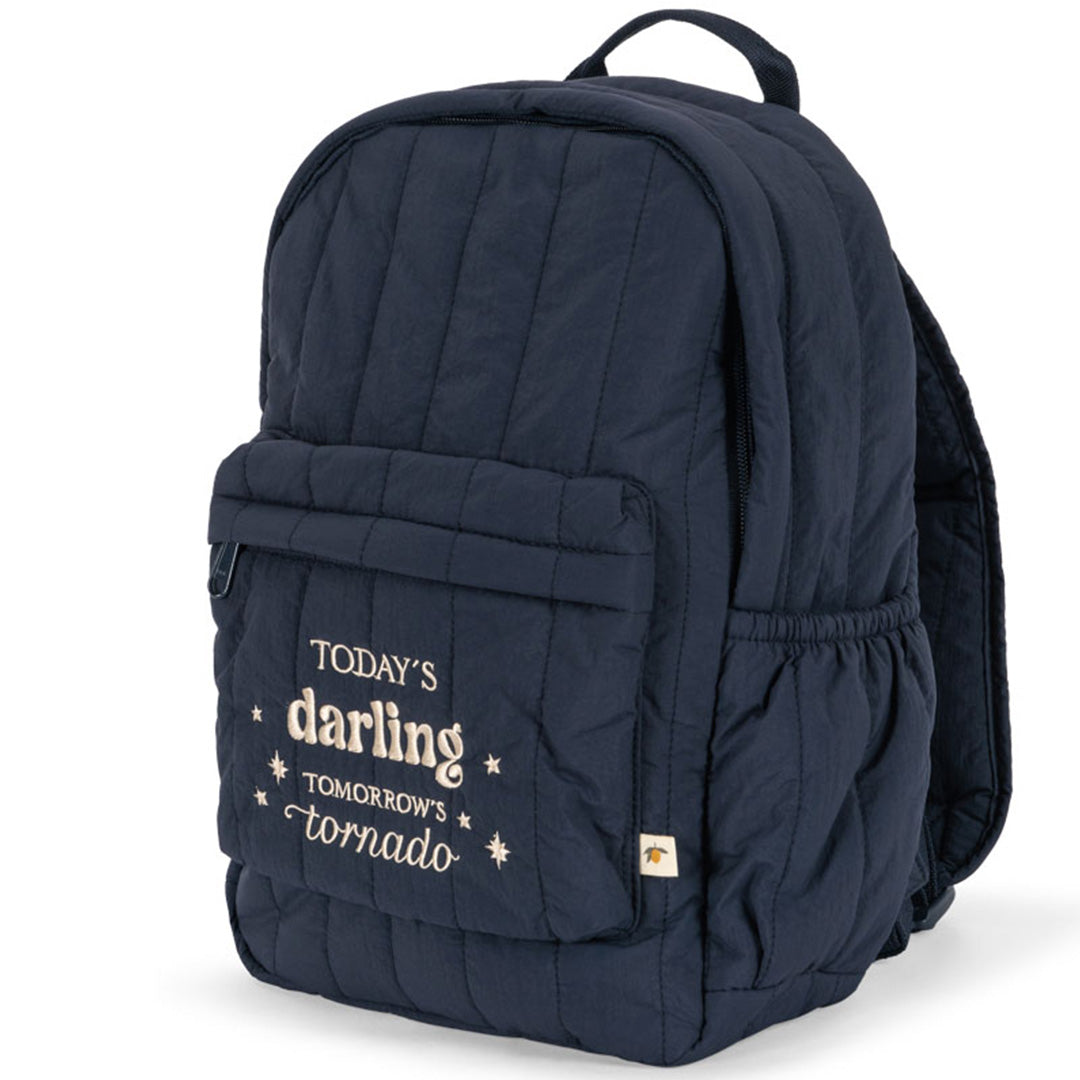 Schuine weergave van de Konges Sløjd marineblauwe gewatteerde schoolrugzak met tekst en sterren, en een zijvak.