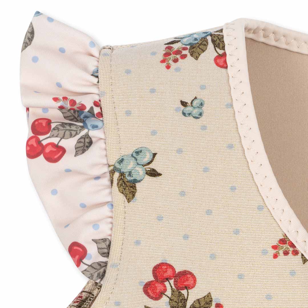 Detail van een Konges Sløjd zwemvest voor kinderen met een gebloemd patroon van kersen en bosbessen en ruches op de schouder.