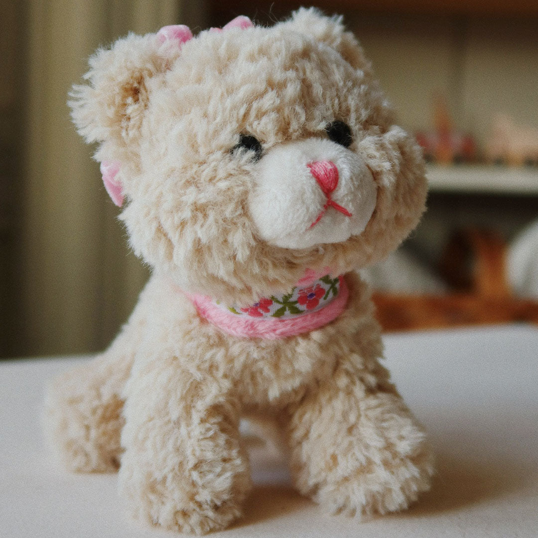 Konges Sløjd beige knuffelpoes met roze strik en gebloemde halsband, van voren gefotografeerd.