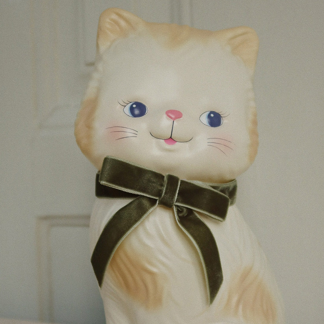 Close-up van de Konges Sløjd kinderlamp, een beige kat met blauwe ogen en een groene fluwelen strik.