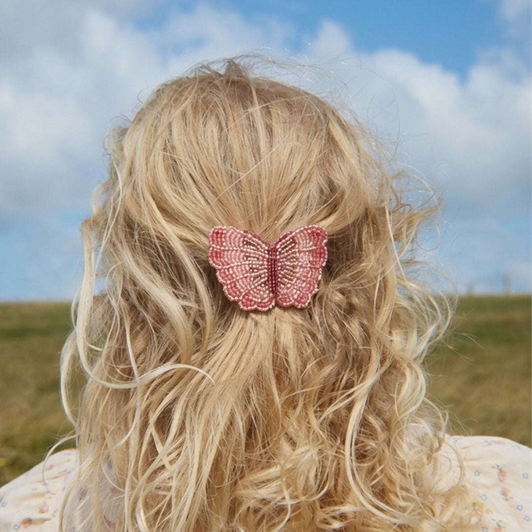 De roze kralen vlinder haarclip zit in het blonde haar van een kind, gezien van achteren.