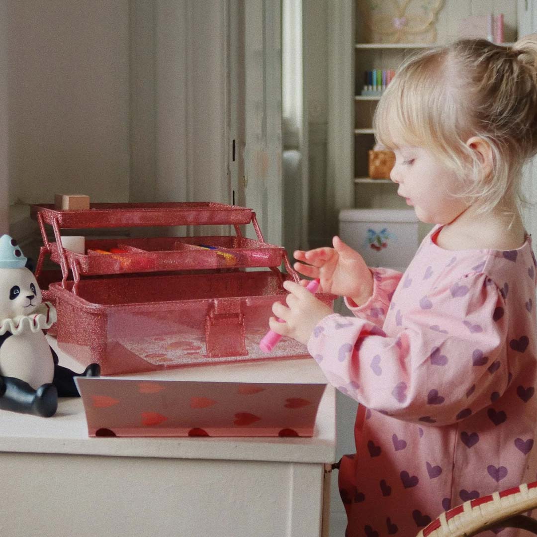 Een kind speelt met de open Konges Sløjd glitter roze knutselset op een tafel.