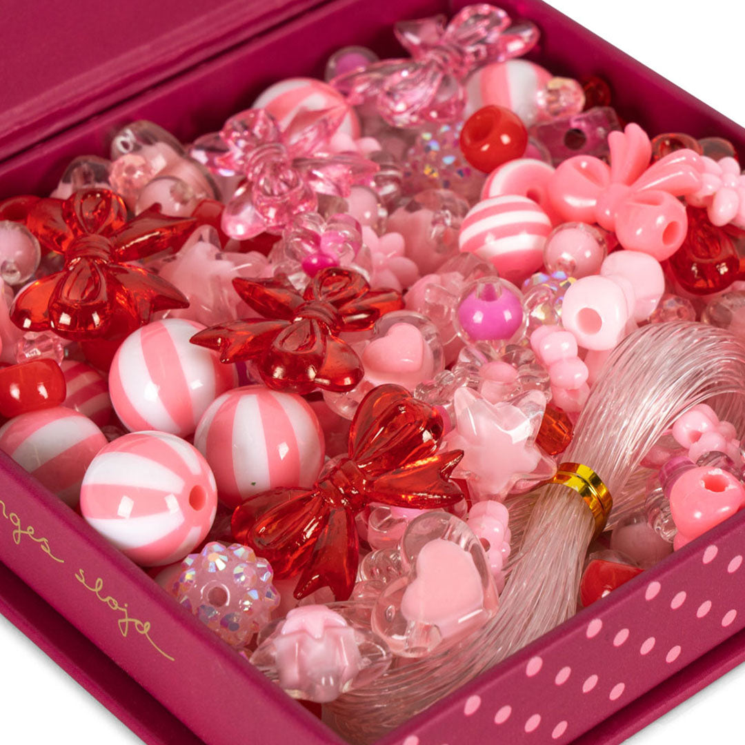Close-up van diverse roze, rode en witte kralen, waaronder strikjes, harten en gestreepte kralen, met roze nylondraad.