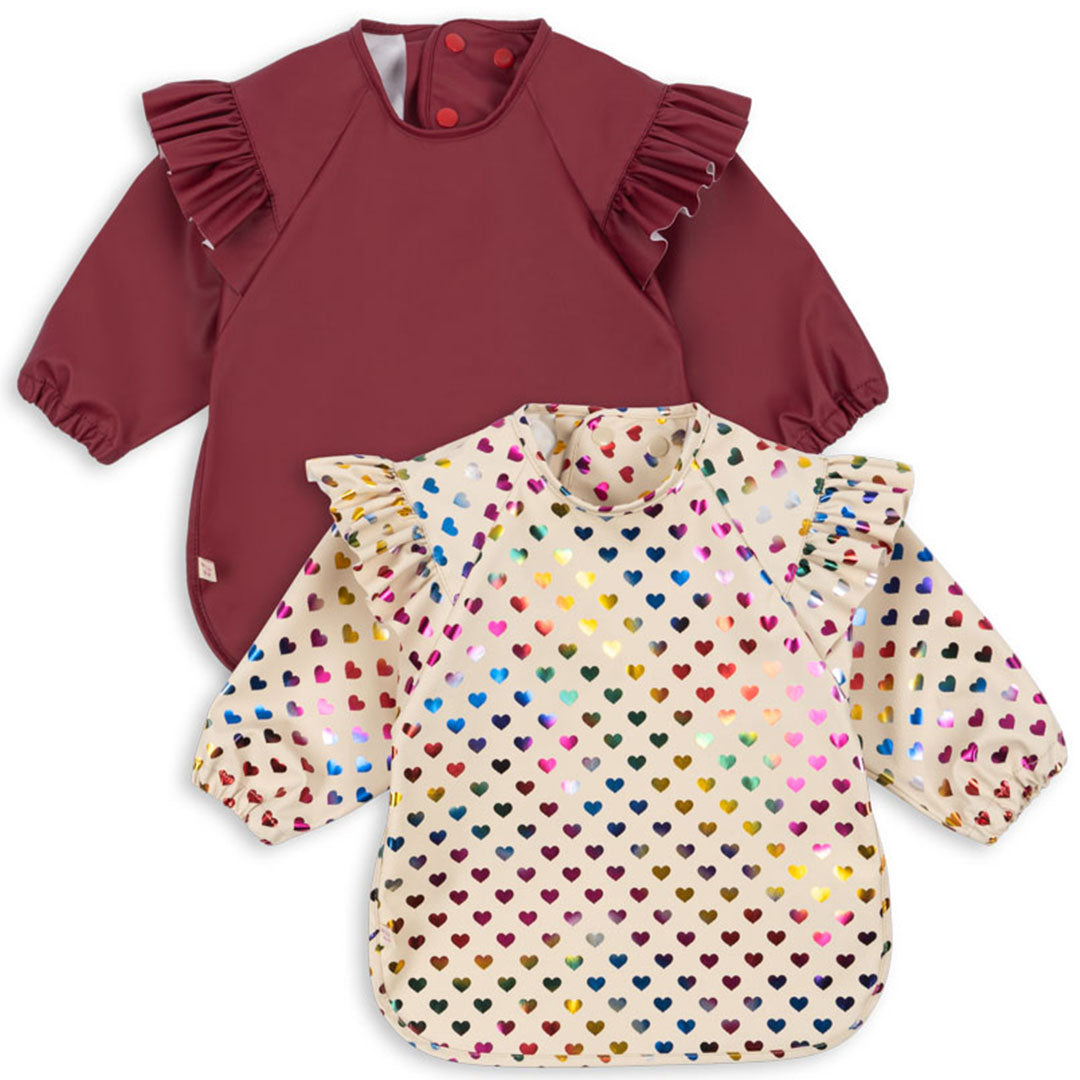 Twee Konges Sløjd mouwslabben voor baby's, één bordeauxrood en één crèmekleurig met kleurrijke glitterharten.