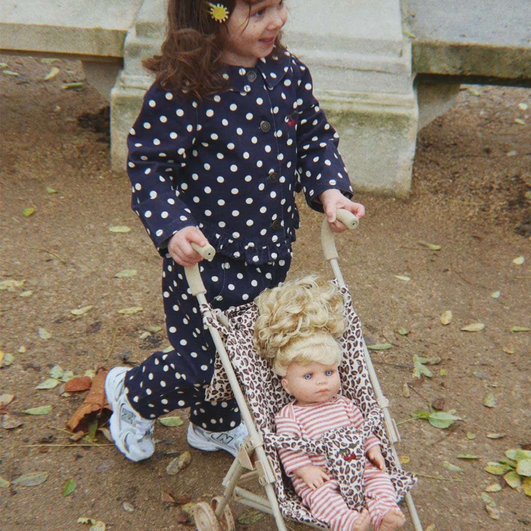 Een kind duwt de Konges Sløjd poppenbuggy met leopard print, waarin een pop zit, over een pad buiten.