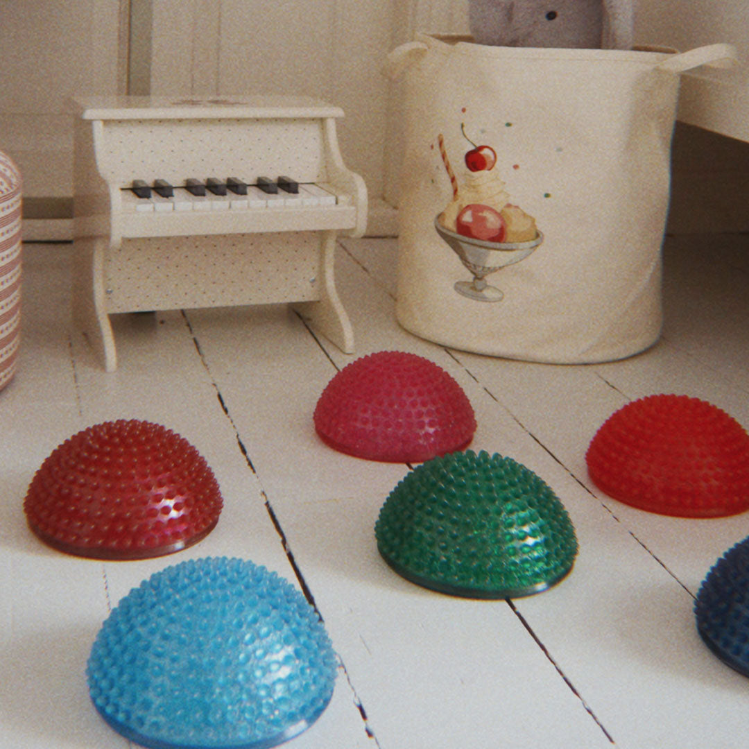 Meerdere konges sløjd sensorische balansstenen liggen op een lichte houten vloer naast een speelgoedpiano.